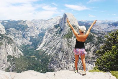 Rear view of young woman standing on mountain against sky