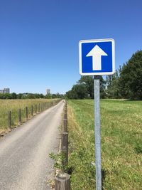 Road sign on field against clear blue sky