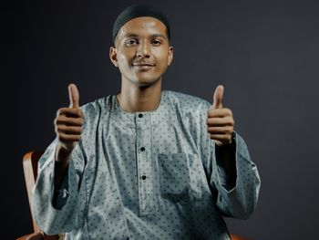 Portrait of young man gesturing while standing against black background