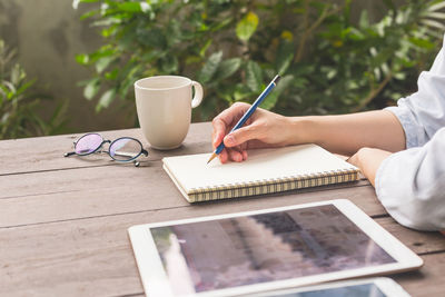 Midsection of woman writing in book at table