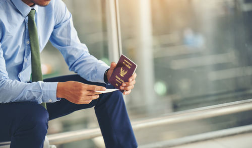 Midsection of man holding passport while sitting in city