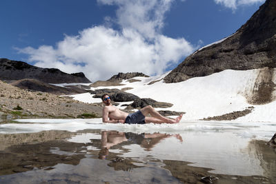 Man lying in lake against mountains during winter