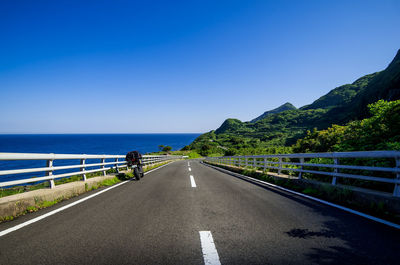 Empty road leading towards sea against blue sky