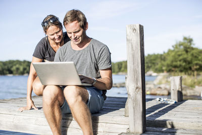 Couple using laptop on pier