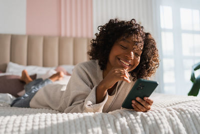 Young woman using mobile phone while sitting on bed at home