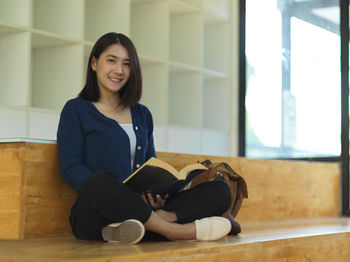 Portrait of smiling young woman sitting on wooden floor