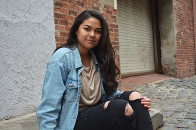 Portrait of young woman sitting on brick wall
