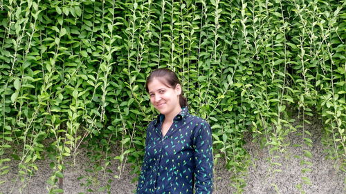 Portrait of young woman standing against plants