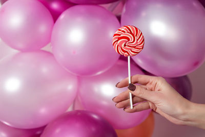 Women's hand holding a round striped candy on the background of pink balloons