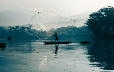 Silhouette man in boat on lake against sky