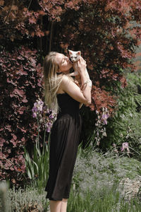 Pretty woman at her 30s in the garden kissing sphinx cat. beautiful dreamlike female walking