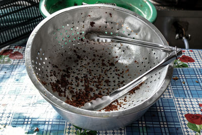 High angle view of tongs in metallic colander on table