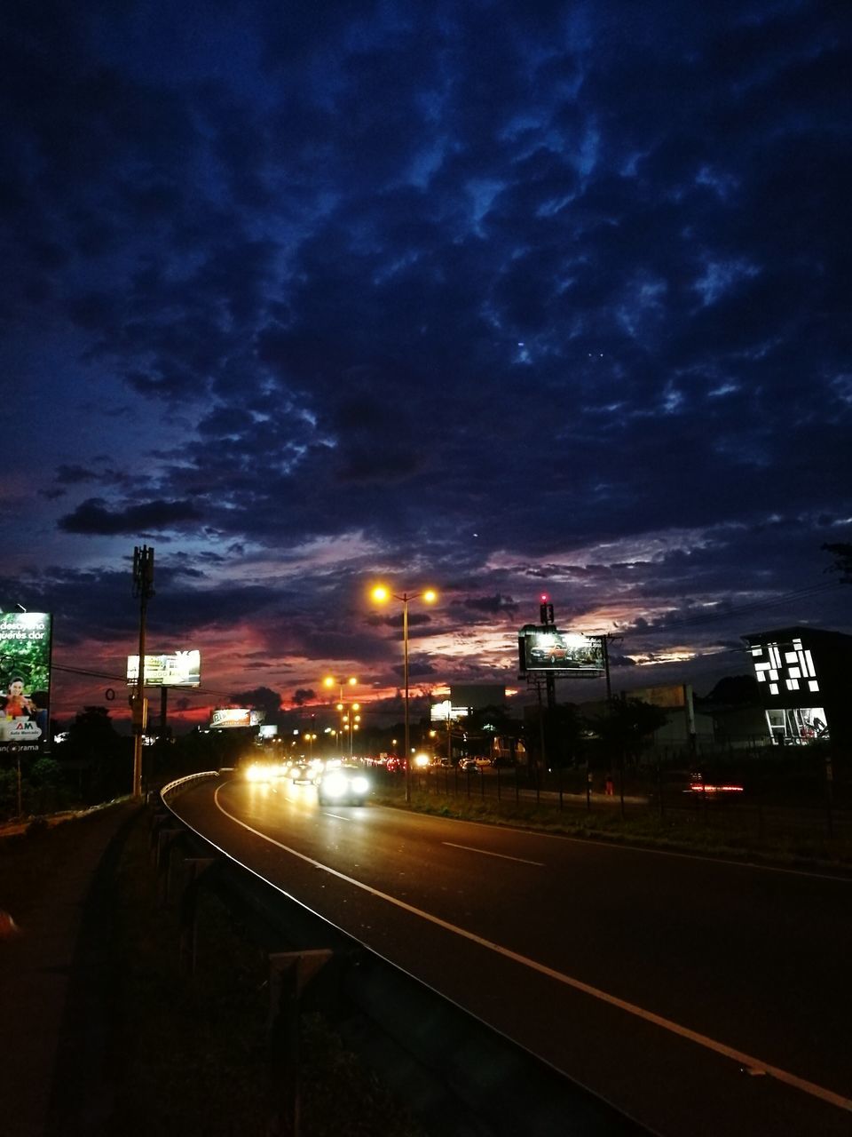 illuminated, sky, night, road, street light, cloud - sky, road marking, the way forward, city, cloudy, outdoors, no people, cloud, city street, city life, diminishing perspective, dark, weather