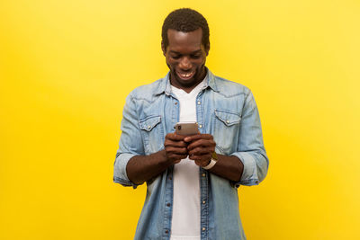 Man holding camera while standing against yellow background