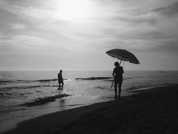 Silhouette people standing on beach against sky
