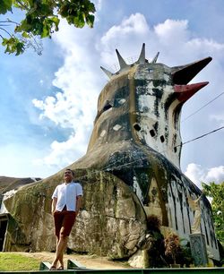 Low angle view of mature man standing by sculpture against sky