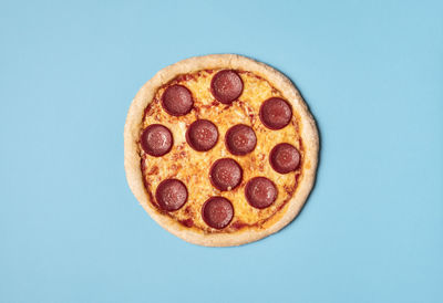 Tasty pizza salami with melted cheese, mozzarella and tomato sauce on a blue background. 