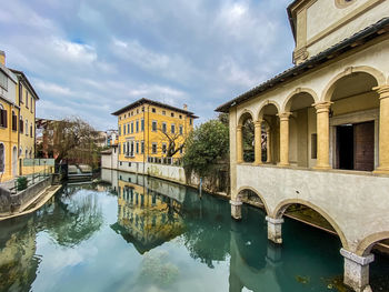 Arch bridge over canal by buildings against sky