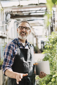 Happy gardener with digital tablet standing in greenhouse