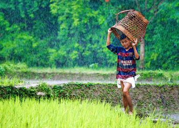 Portrait of boy holding basket while standing on field during rainfall