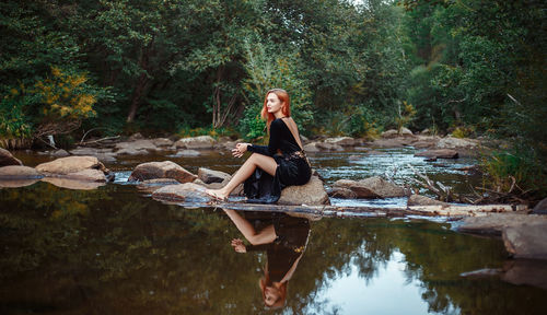 Young woman sitting at lakeshore in forest