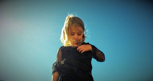 Low angle view of girl standing against clear blue sky