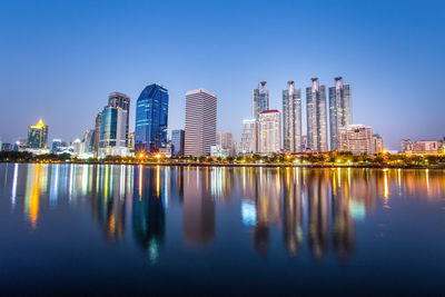 Illuminated buildings by river against clear sky