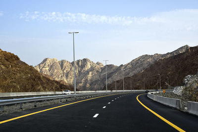 Empty road by mountains against sky