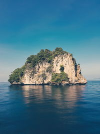 Rock formation in sea against clear blue sky