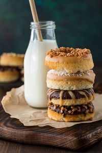 A stack of homemade donuts with various toppings and a bottle of milk in behind.