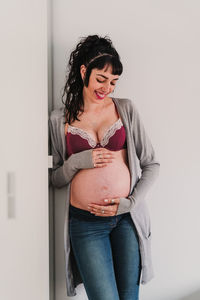 Pregnant woman in bra standing against wall