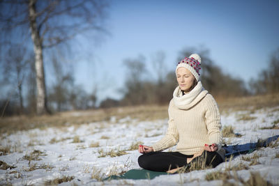 Young athletic woman sitting and meditatingin the yoga pose on the snowy field during winter 