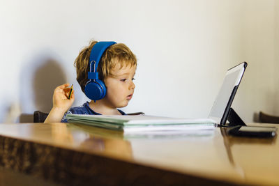 Rear view of boy using mobile phone while sitting on table