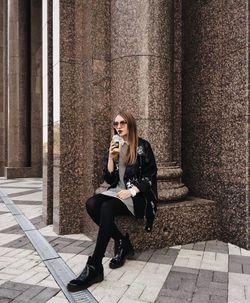 Full length of woman sitting on sidewalk in city