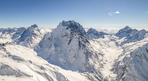 Peaks of the mountain range under the snow above the clouds