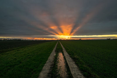 Road amidst field against sky during sunset