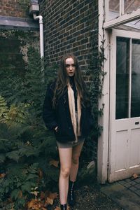 Portrait of young woman standing against brick wall