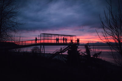 Intense pink, purple, blue sunset with people on bridge over railway going to beach