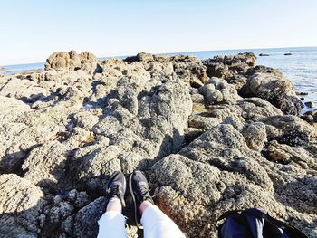 Low section of person on rocks by sea against clear sky