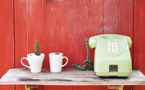 Close-up of telephone by potted plants on shelf against red wall