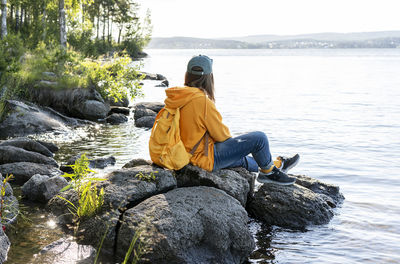 Rear view of man sitting on rock by lake