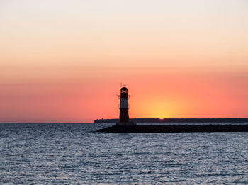 Lighthouse by sea against sky during sunset