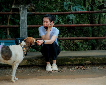 Full length of young woman with mask feeding dog outdoors