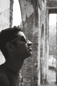 Profile view of thoughtful man wearing sunglasses while leaning on wall