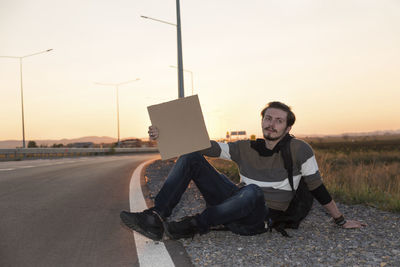 Man sitting by road against sky