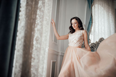 Full length of happy woman standing against curtain