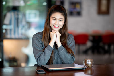Portrait of smiling woman with laptop and coffee on table sitting in cafe