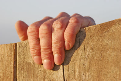 Close-up of human hand gripping onto wooden surface