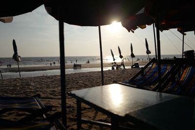 Chairs and table at beach against sky during sunset