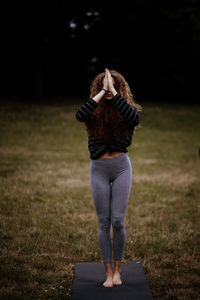 Rear view of woman standing in park whilst meditating and holding her hands together